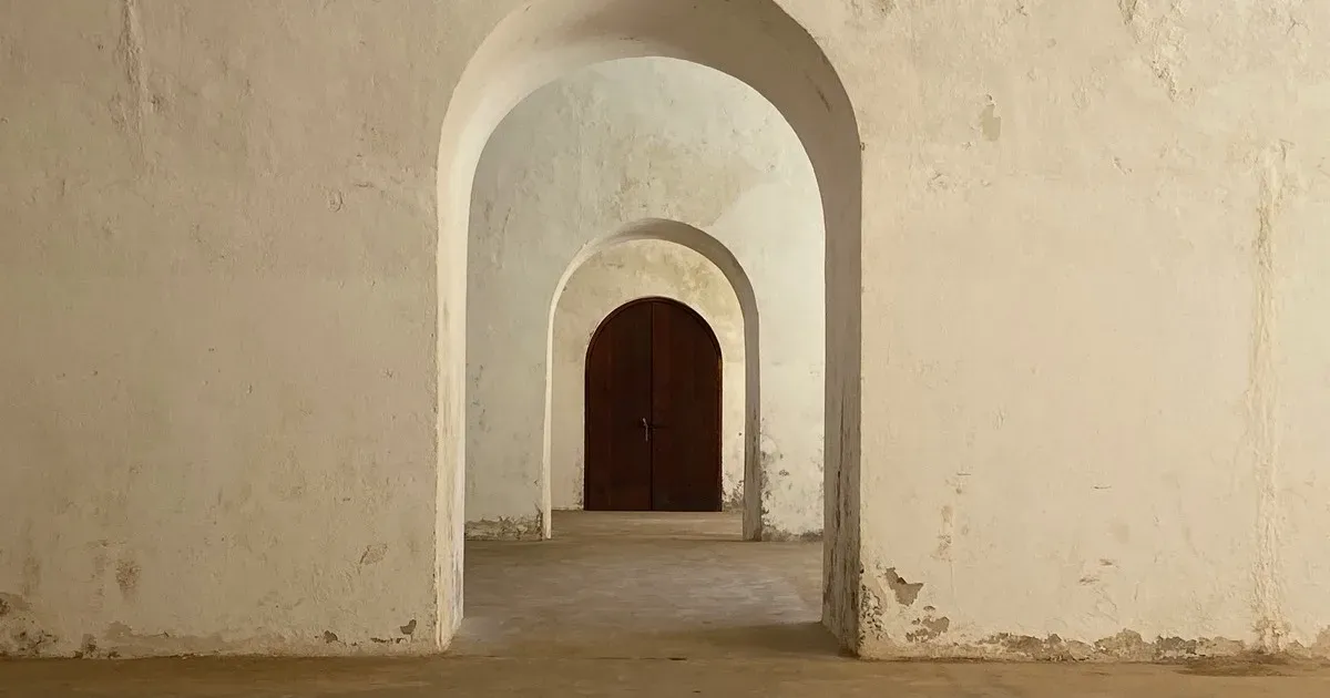 A series of whitewashed archway doorways receding toward a closed wooden door