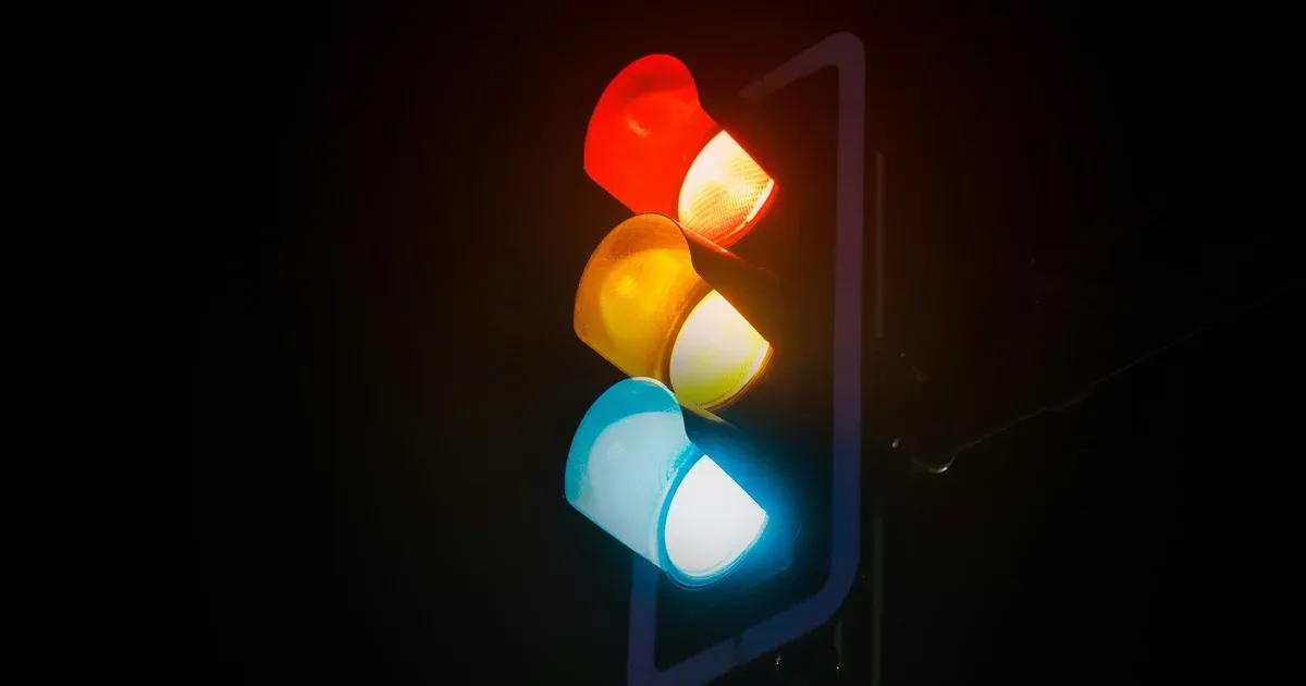 A traffic light glowing red, yellow, and green all at once against a black night sky