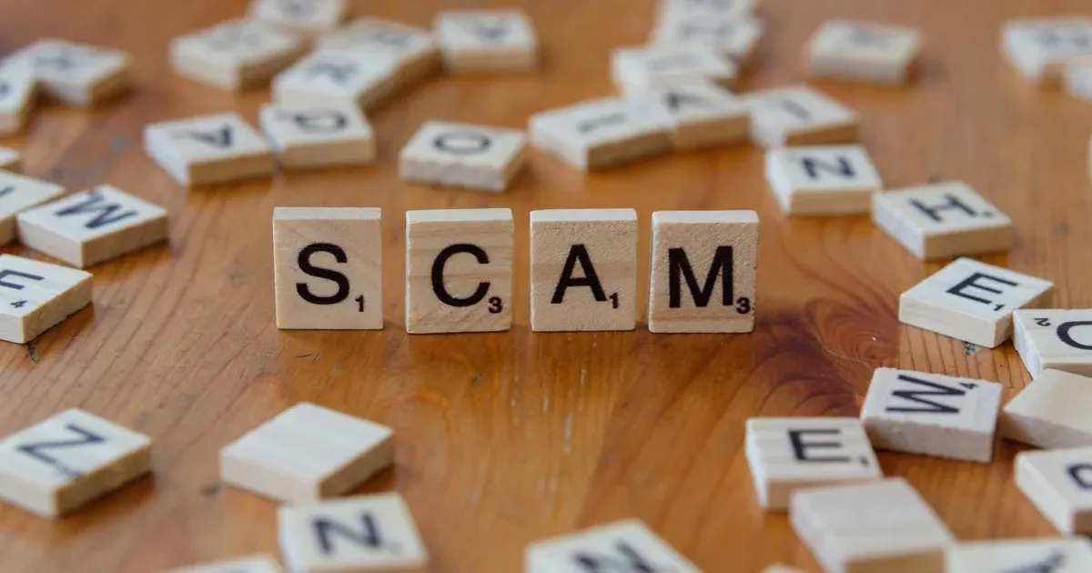 Wooden Scrabble tiles arranged to spell the word SCAM on a table